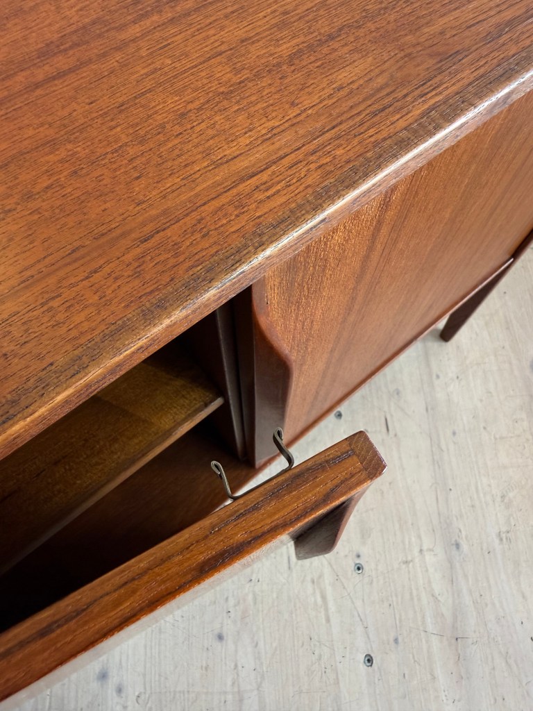 Close-up view of a wooden furniture piece with a polished finish, featuring an open drawer with metal pull handles.