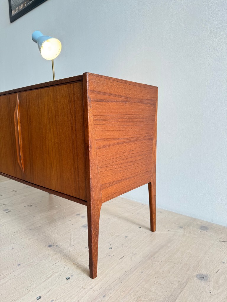 Close-up of a mid-century wooden sideboard with tapered legs and a modern lamp on top.