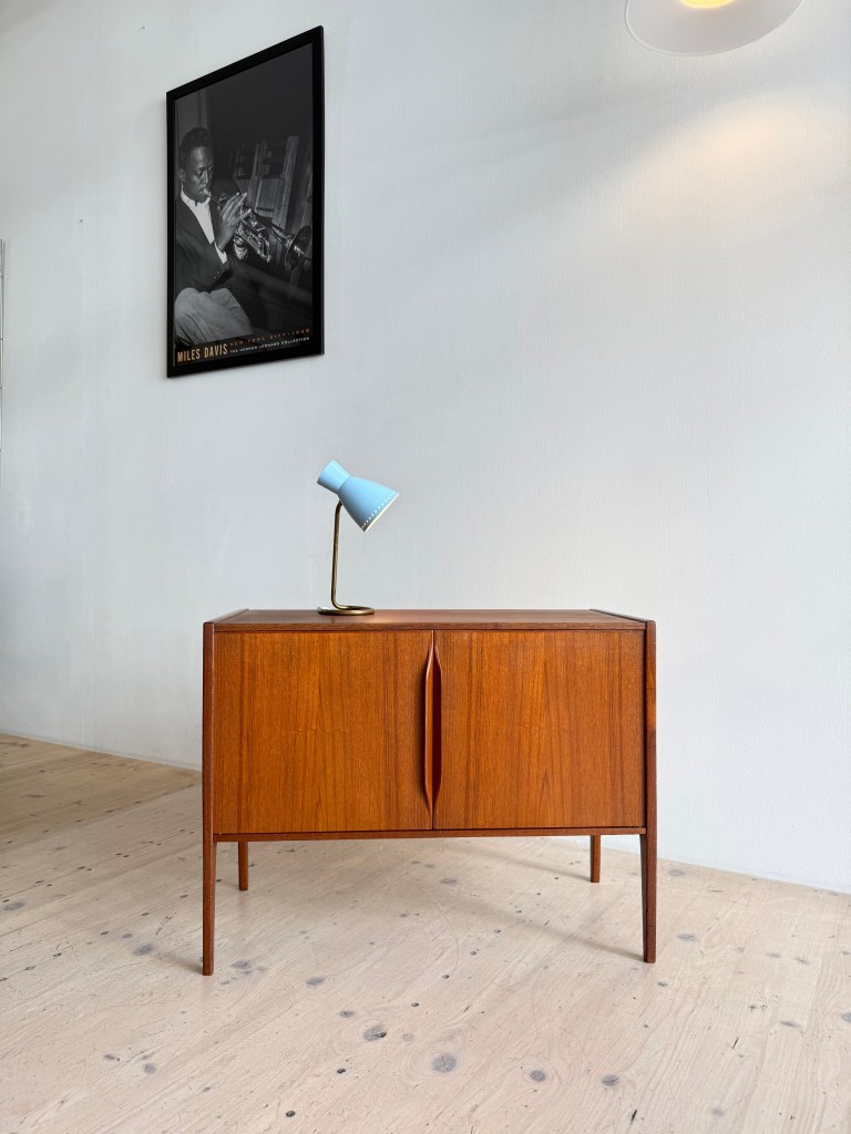A wooden sideboard with two doors, featuring a stylish blue lamp on top, set against a minimalistic wall with a black and white image of a musician.