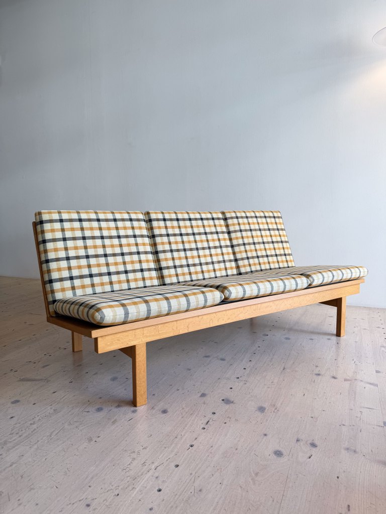 A mid-century modern sofa with a wooden frame and plaid upholstery in beige, brown, and black.