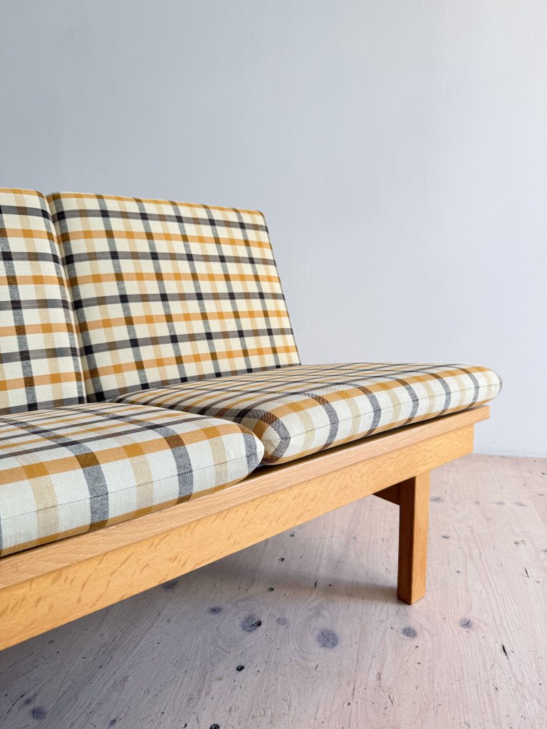 A close-up view of a mid-century modern sofa featuring a plaid fabric design in yellow, beige, and black tones, with a light wooden frame.