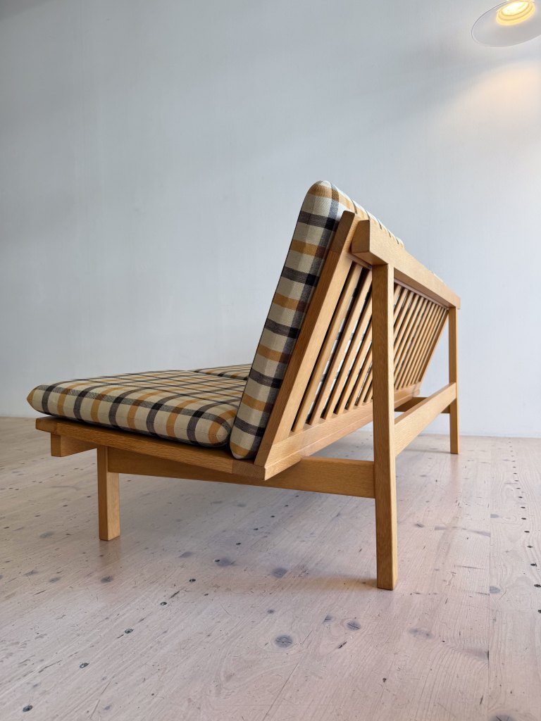 A wooden bench with a plaid cushion, showing a side view and set against a simple background.