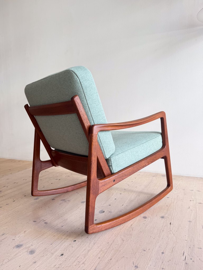 A mid-century modern rocking chair with a wooden frame and light green upholstered seat and backrest.