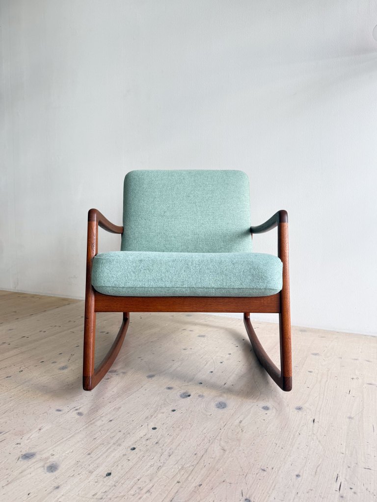 A modern light green upholstered rocking chair with wooden armrests and legs, set against a minimalist background.