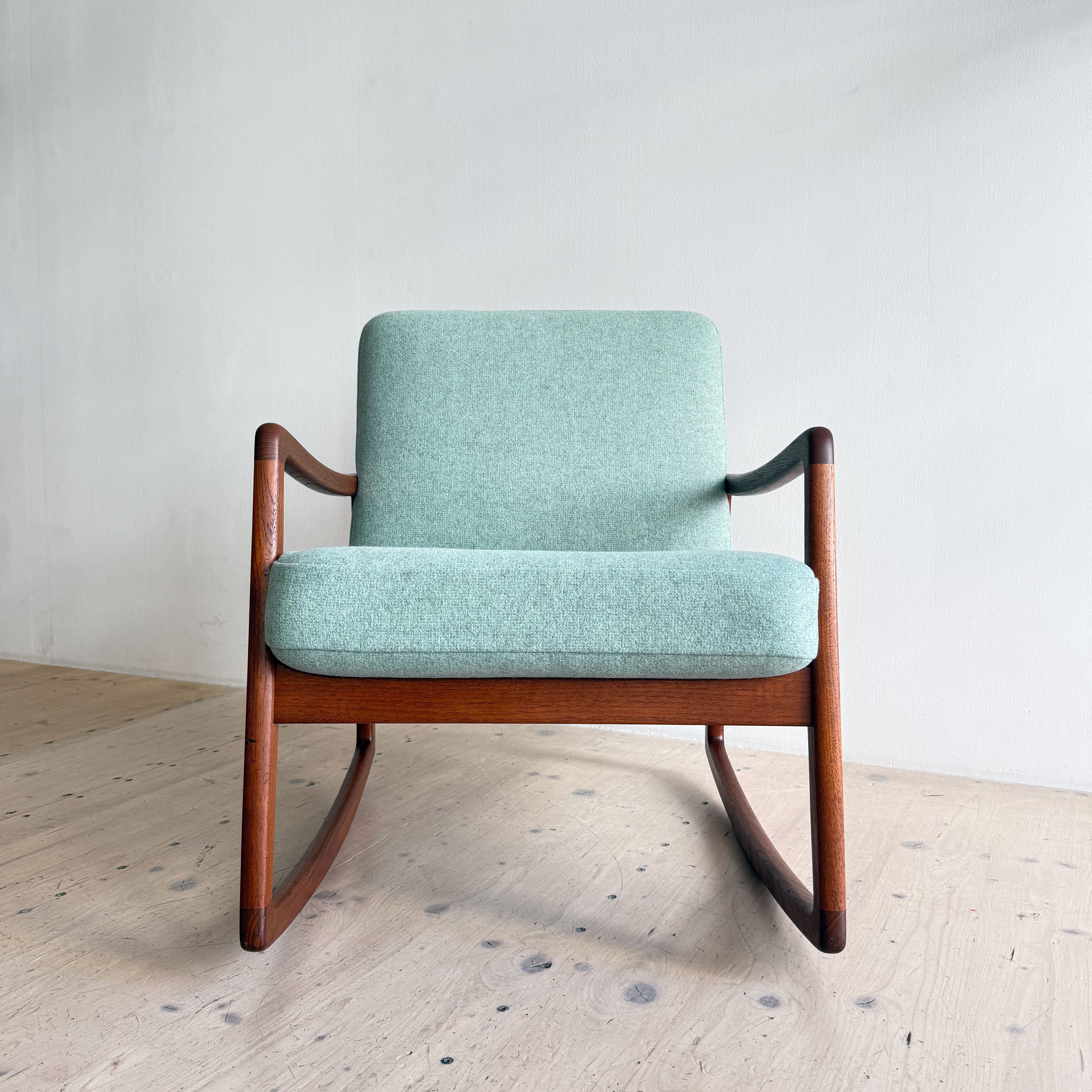 A mint green upholstered rocking chair with wooden arms and frame, set against a neutral wall.