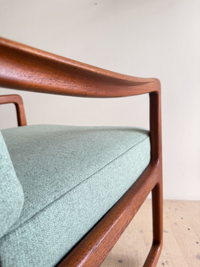 Close-up view of a mid-century modern chair featuring a wooden armrest and a soft green upholstered seat.