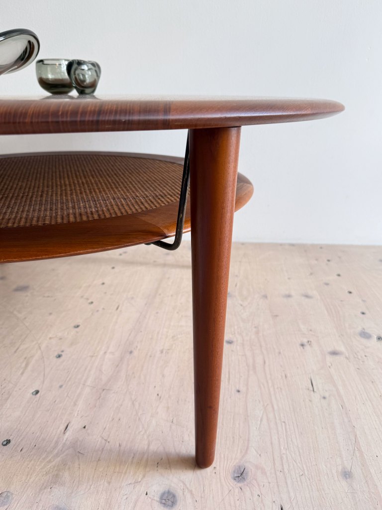Close-up of a mid-century modern wooden coffee table with tapered legs and a woven lower shelf, displaying a few metallic decorative items on top.
