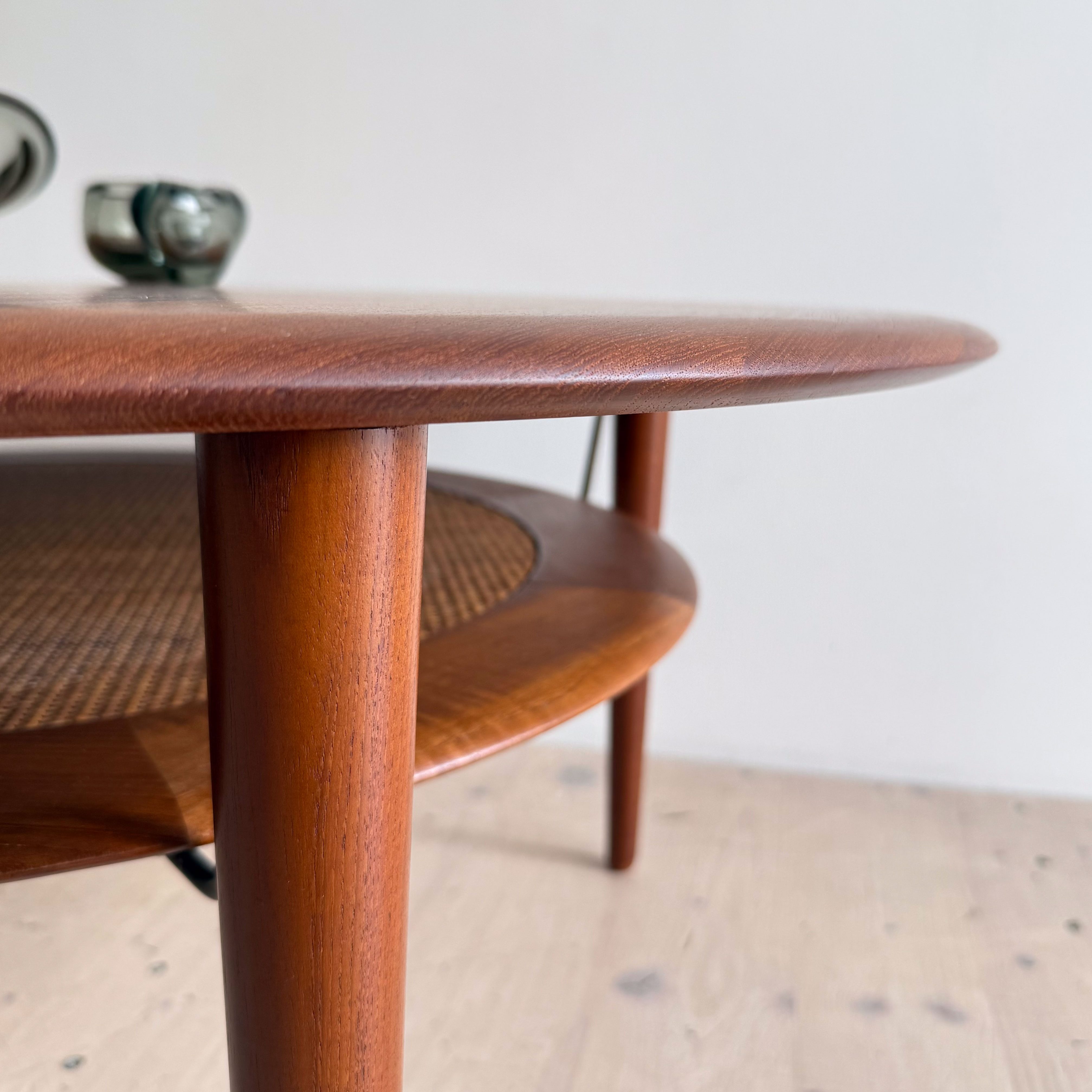 A close-up view of a mid-century modern coffee table with a round wooden top and graceful, slender legs, featuring a woven shelf underneath.