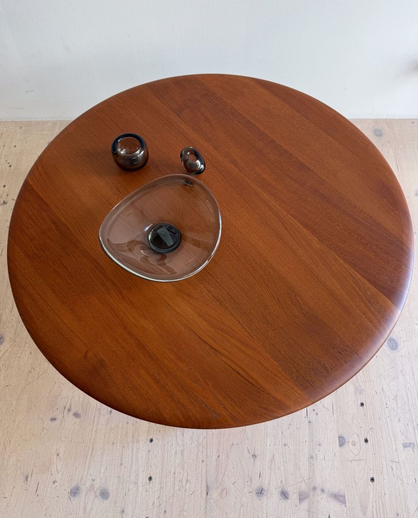 A top view of a round wooden table featuring a glass dish and two small black decorative items.