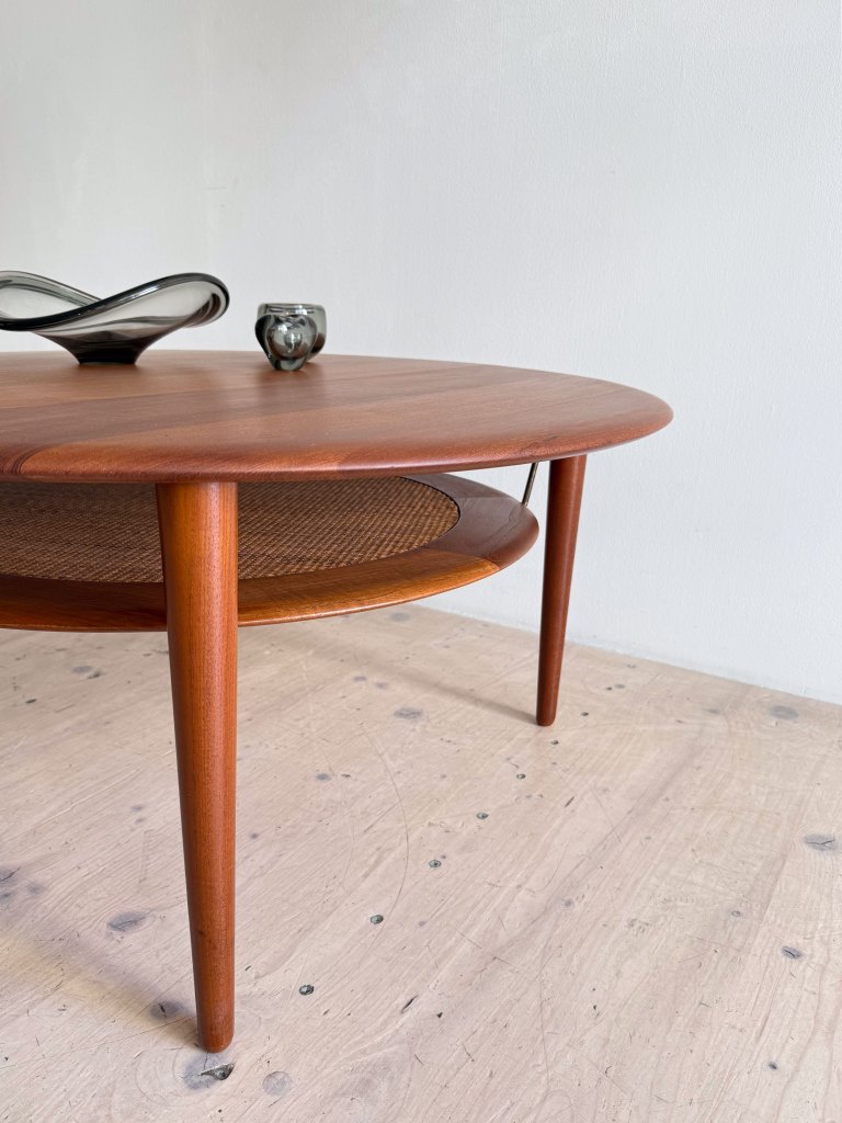 Mid-century modern wooden coffee table with tapered legs, featuring a round top and woven shelf, decorated with a glass bowl and a small candle holder.