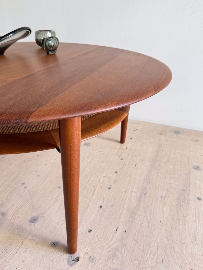 Close-up view of a round wooden coffee table with thin legs and a lower shelf, featuring decorative items on top.