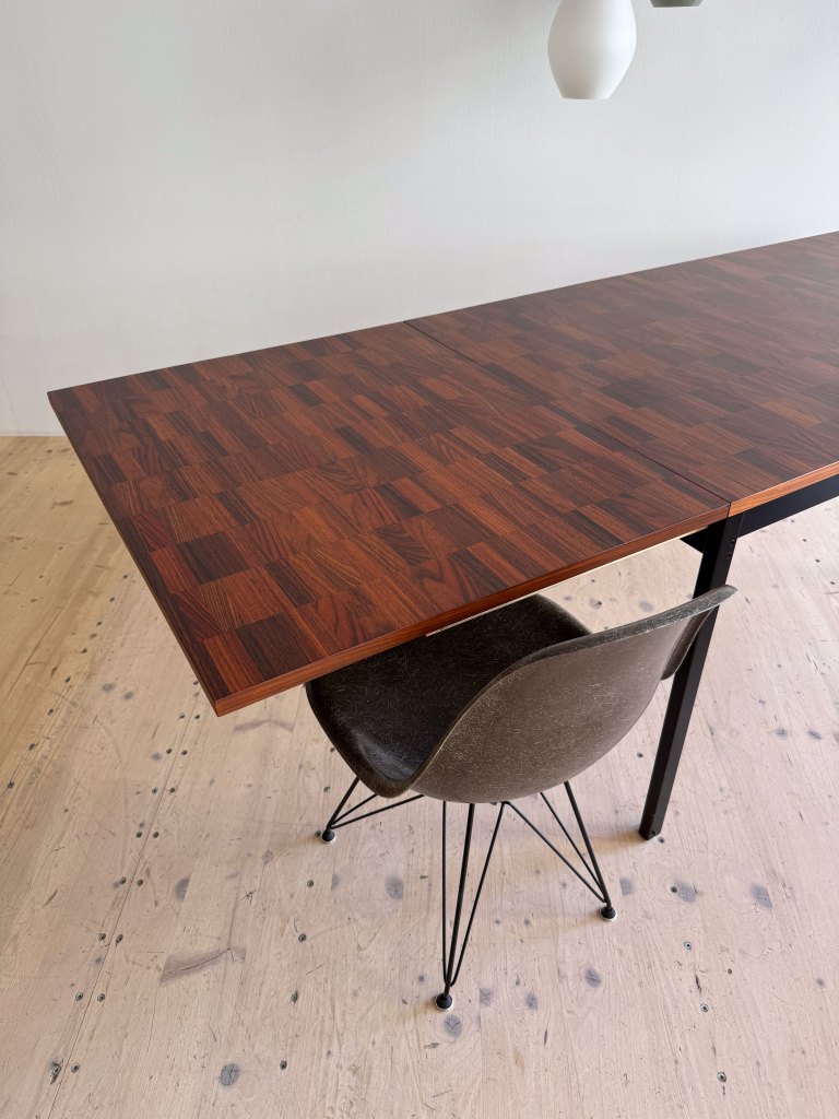 A wooden dining table with a rich, dark finish and a modern chair next to it, set against a neutral wall.