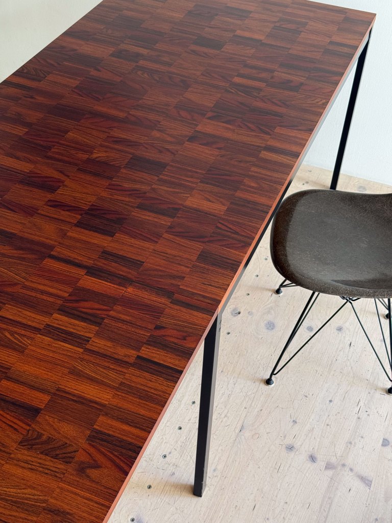 A close-up view of a wooden dining table with a rich, patterned dark finish, accompanied by a modern chair with a black frame and a cushioned seat.