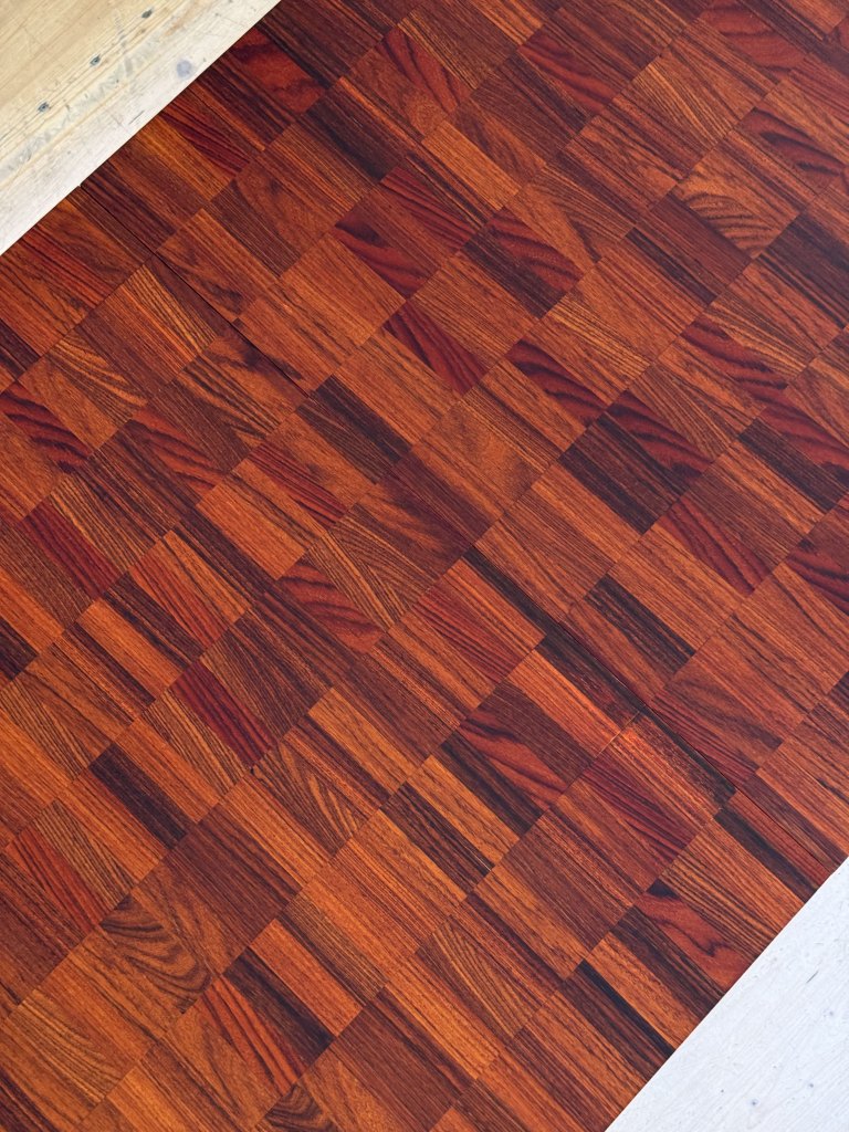 A close-up view of a patterned wooden floor featuring reddish-brown parquet blocks with varying shades and textures.