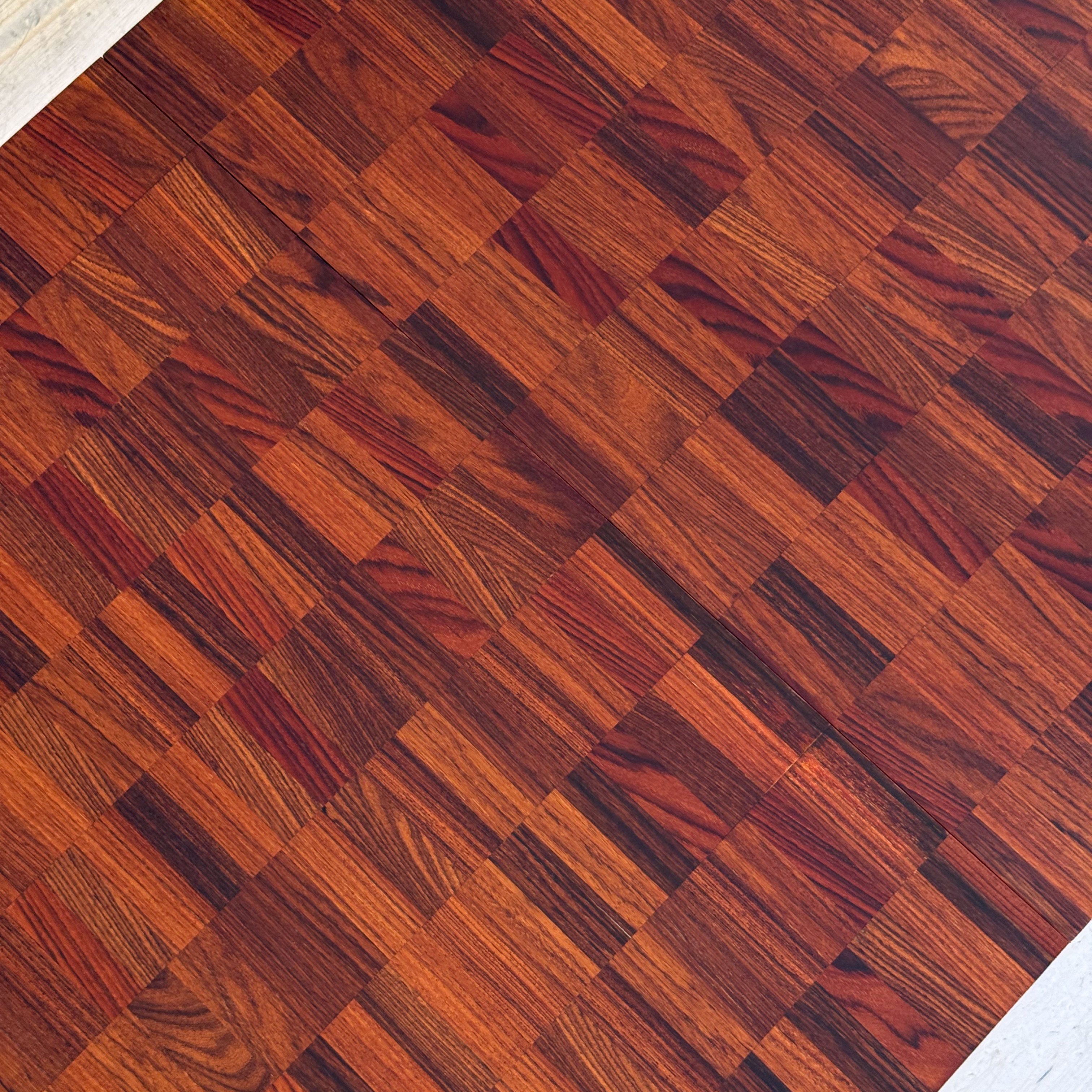 Close-up view of a wooden floor with a patterned arrangement of rich, reddish-brown parquet tiles.