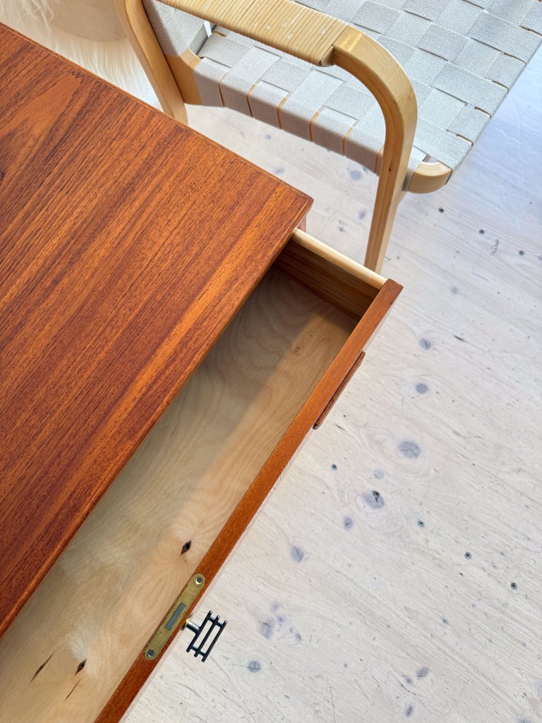 Close-up view of an open wooden drawer with a polished surface, revealing smooth wood inside, alongside a stylish woven chair.