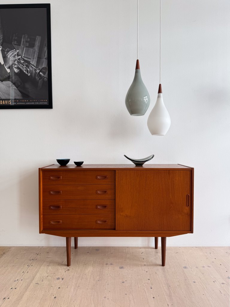 A stylish wooden sideboard with multiple drawers, accompanied by decorative bowls and two pendant lights hanging above it, against a white wall.