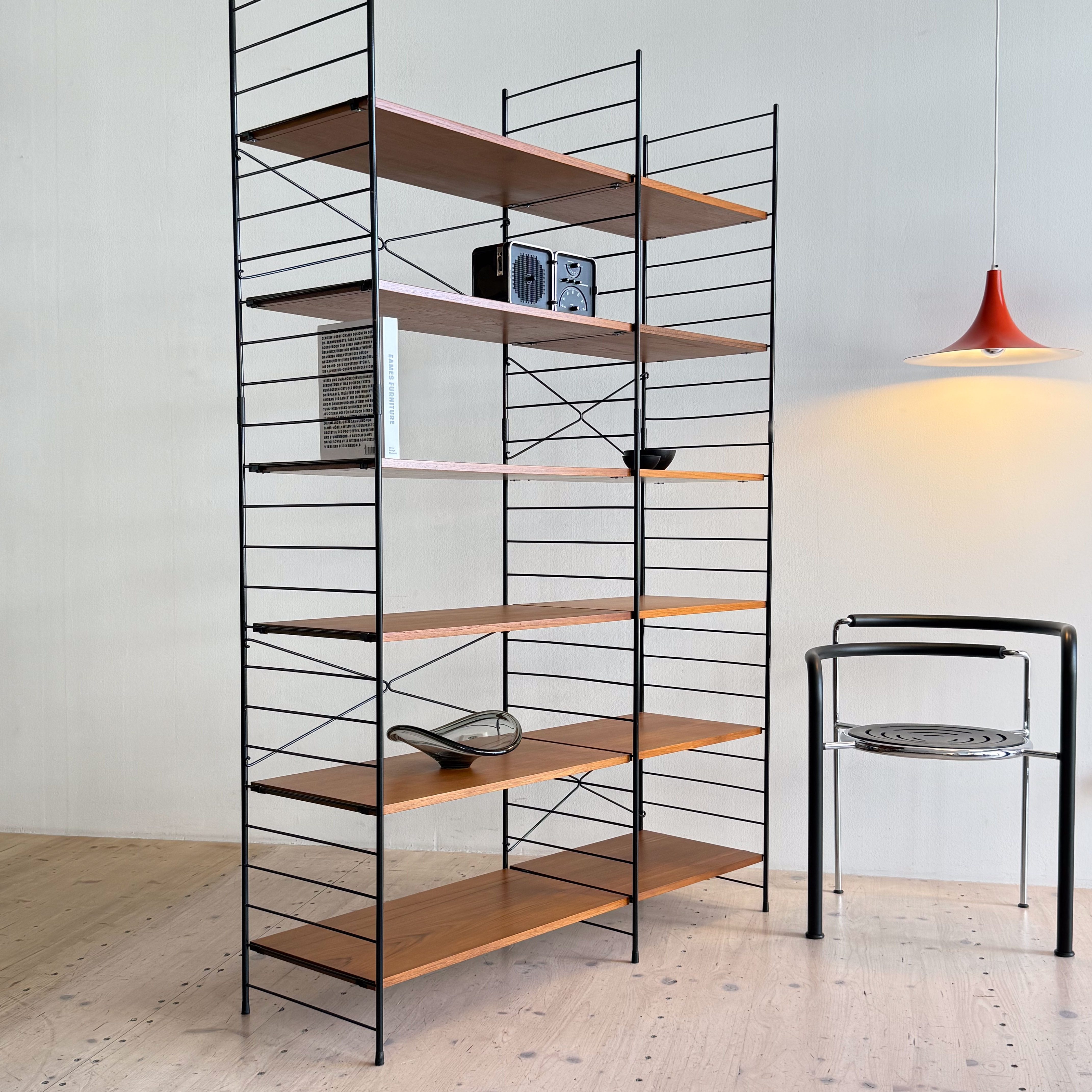 A modern black metal bookshelf with wooden shelves displaying a few items, including books, a retro radio, and a decorative object. A minimalist chair is positioned nearby.