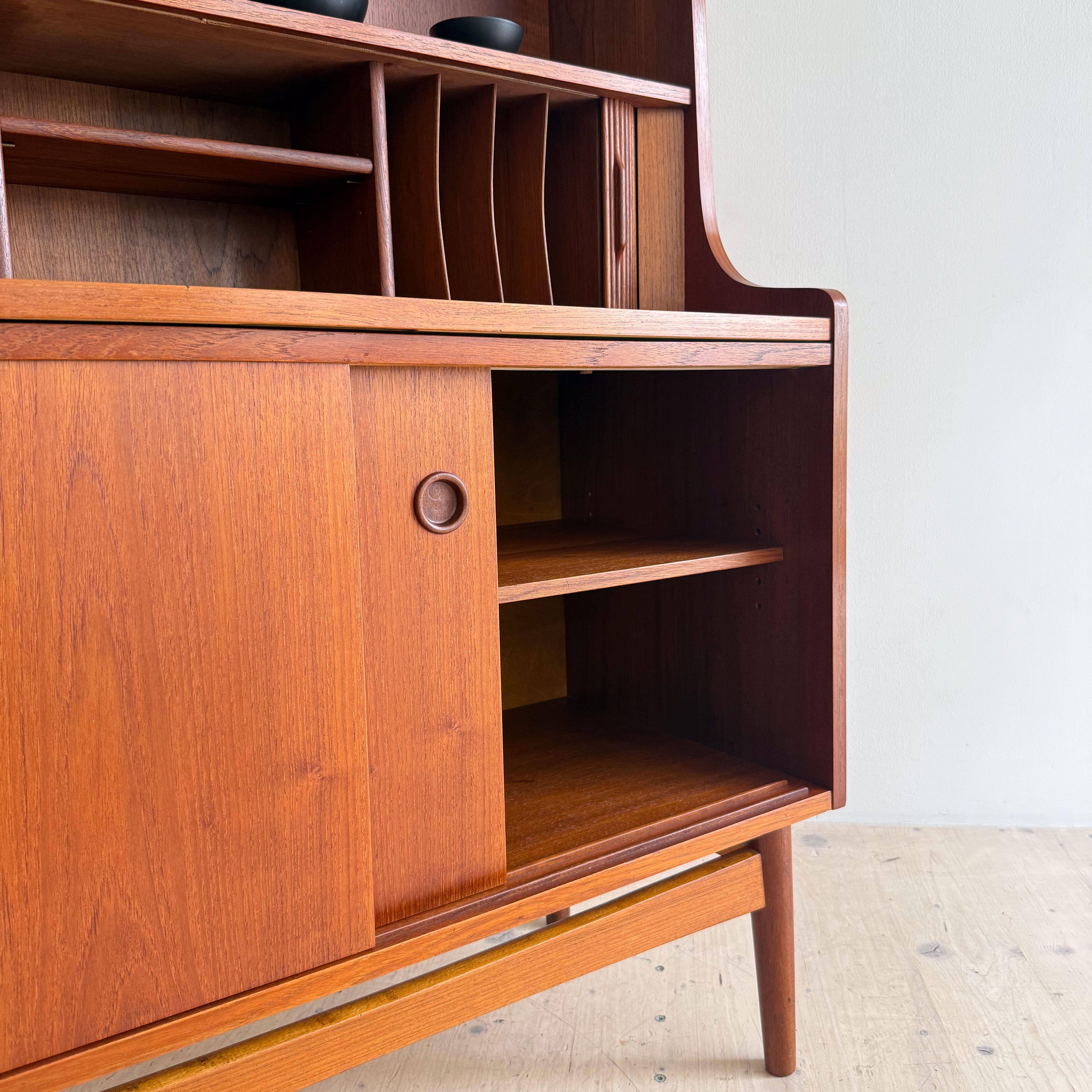 Close-up view of a wooden mid-century modern cabinet featuring shelves, cabinets, and two black decorative bowls on top.