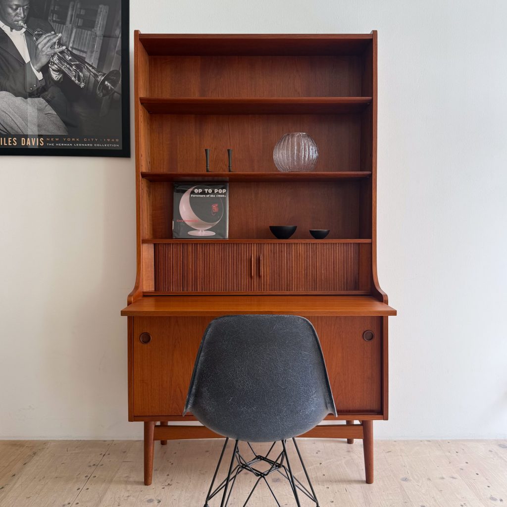 Mid-century modern wooden desk with open shelves, featuring a black chair and decorative items on the shelves.
