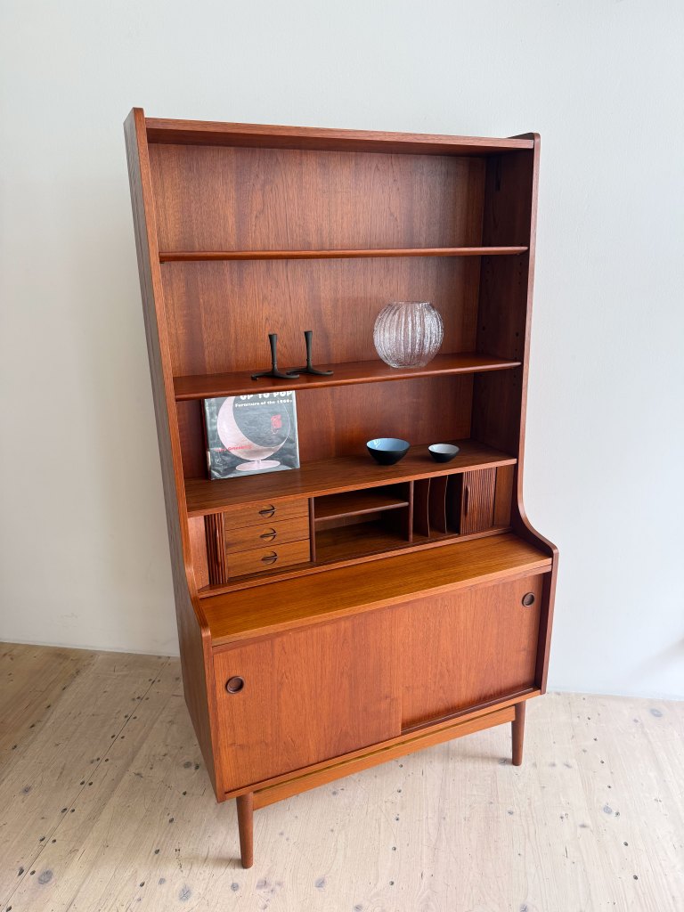 A mid-century modern wooden cabinet with shelves, featuring decorative items including a vase, cups, and a book.