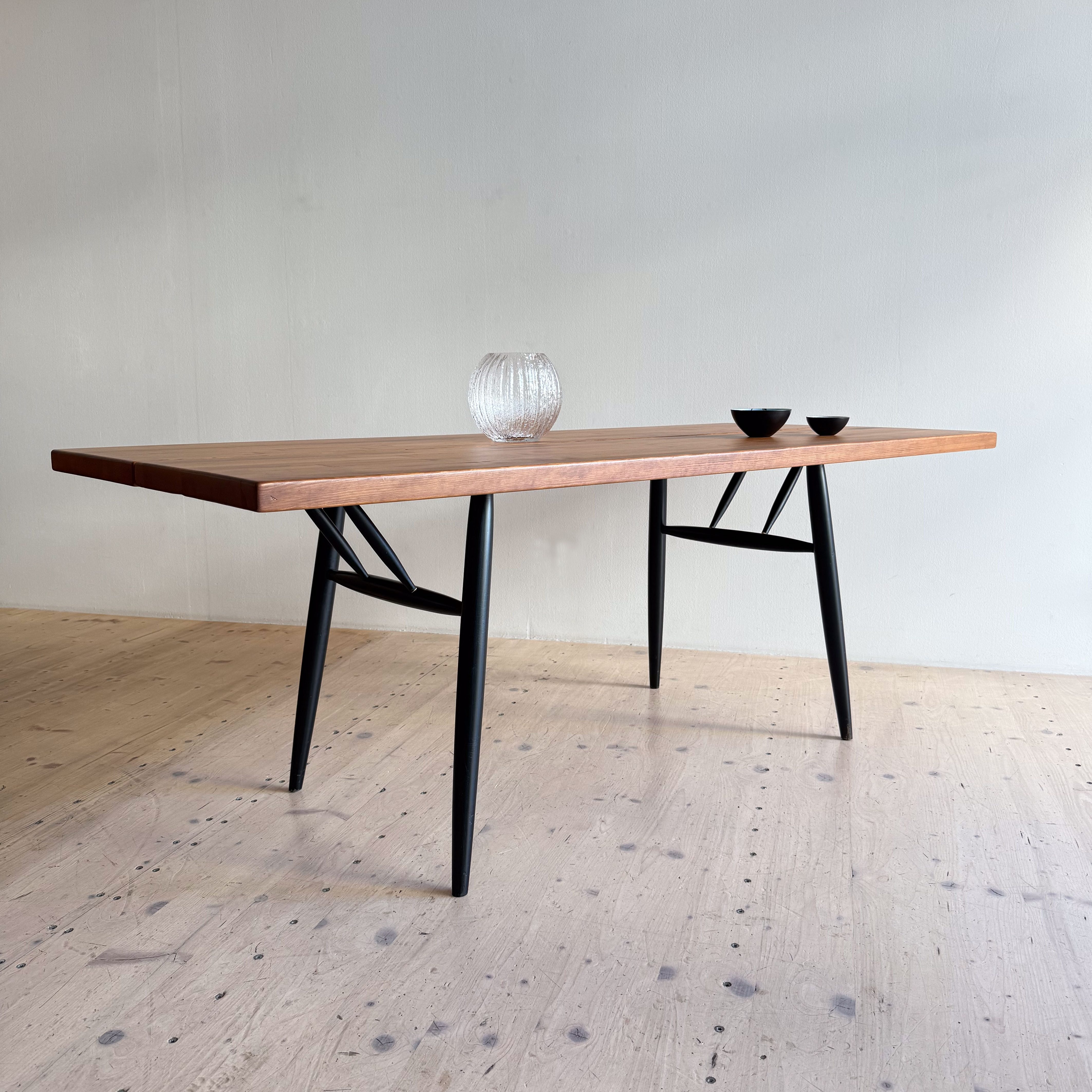 A modern dining table with a wooden top and black metal legs, featuring a glass vase and two small bowls on its surface.