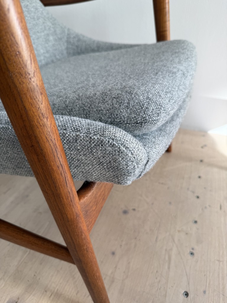 Close-up of a mid-century modern chair featuring a gray fabric seat and wooden legs.