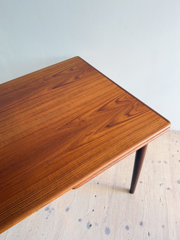 Close-up of a wooden tabletop with a smooth, polished finish and a subtle grain pattern, resting on a light-colored floor.