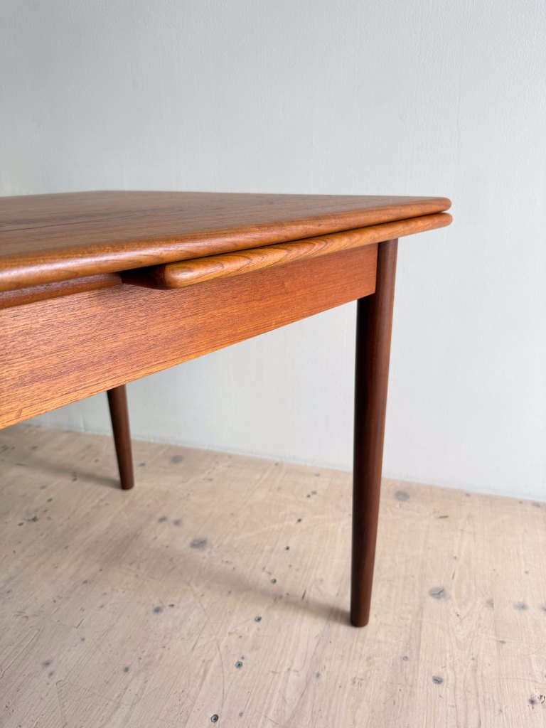 A close-up view of a mid-century wooden table with a smooth finish and tapered legs, set against a light-colored wall.