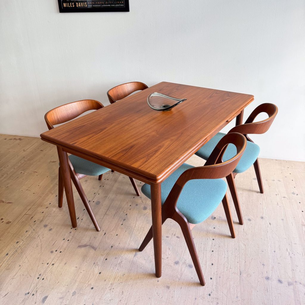 A wooden dining table with a smooth finish surrounded by four stylish chairs featuring light blue upholstery.