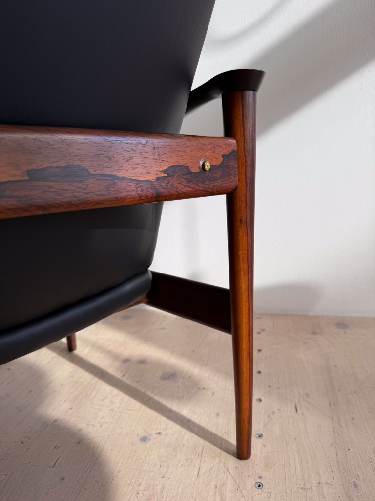 A close-up view of a stylish armchair showcasing a black upholstered seat and wooden armrest with a decorative brass detail.