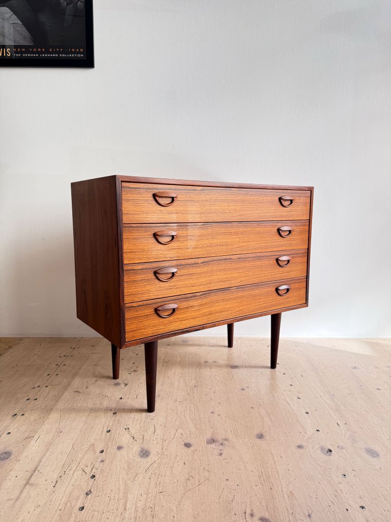 A mid-century modern wooden dresser with five drawers and tapered legs, displayed on a light wooden floor.