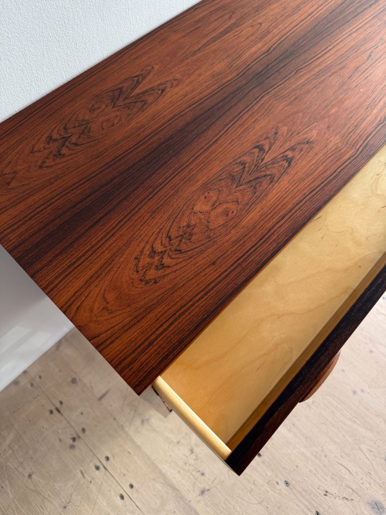 Close-up view of a wooden table top featuring a rich, dark grain pattern, with a partially opened drawer showcasing a lighter wood interior.