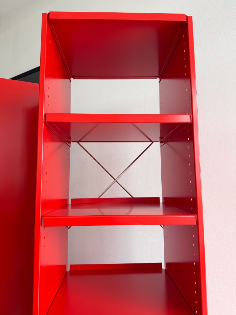 A bright red metal shelf with three open compartments, featuring a cross-bracing design for stability.
