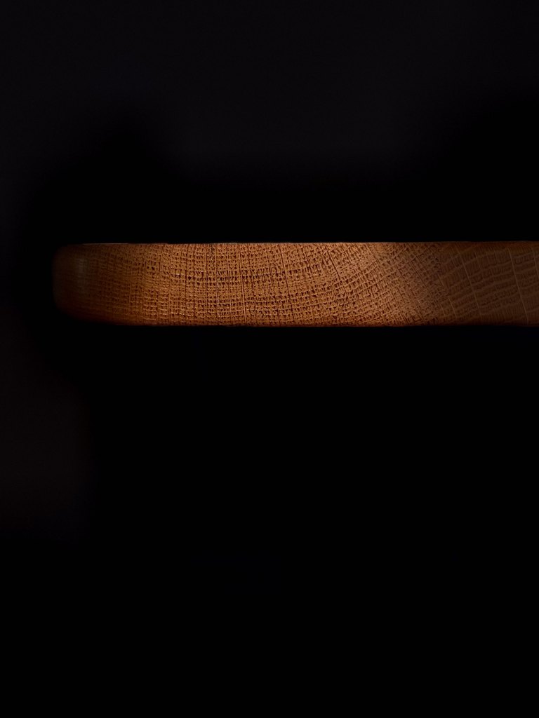 A close-up view of a wooden bowl rim against a dark background, highlighting its texture and color.