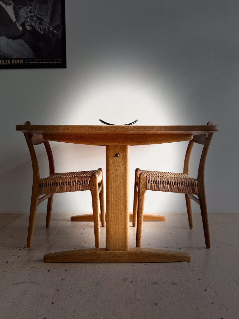 A wooden dining table with two chairs around it, illuminated by soft light, set against a neutral wall.