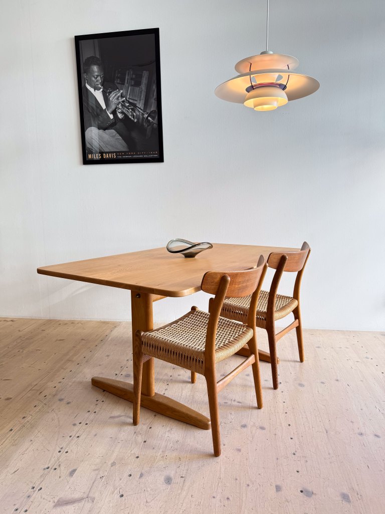 A wooden dining table with two chairs, a modern pendant light, and a framed black-and-white photograph of a man playing the trumpet on the wall.
